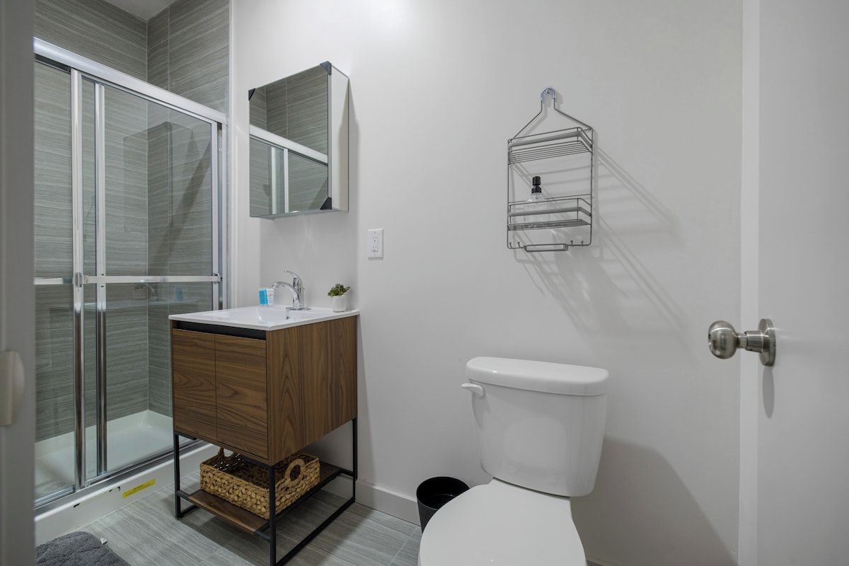 Een badkamer met een douchecabine van glas, een houten wastafelmeubel met een wastafel, een toilet en een handdoekhouder aan de muur.