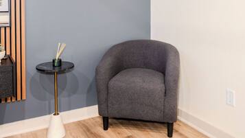 A room with a grey armchair, a small round table with a black top and gold legs, and a white conical base.