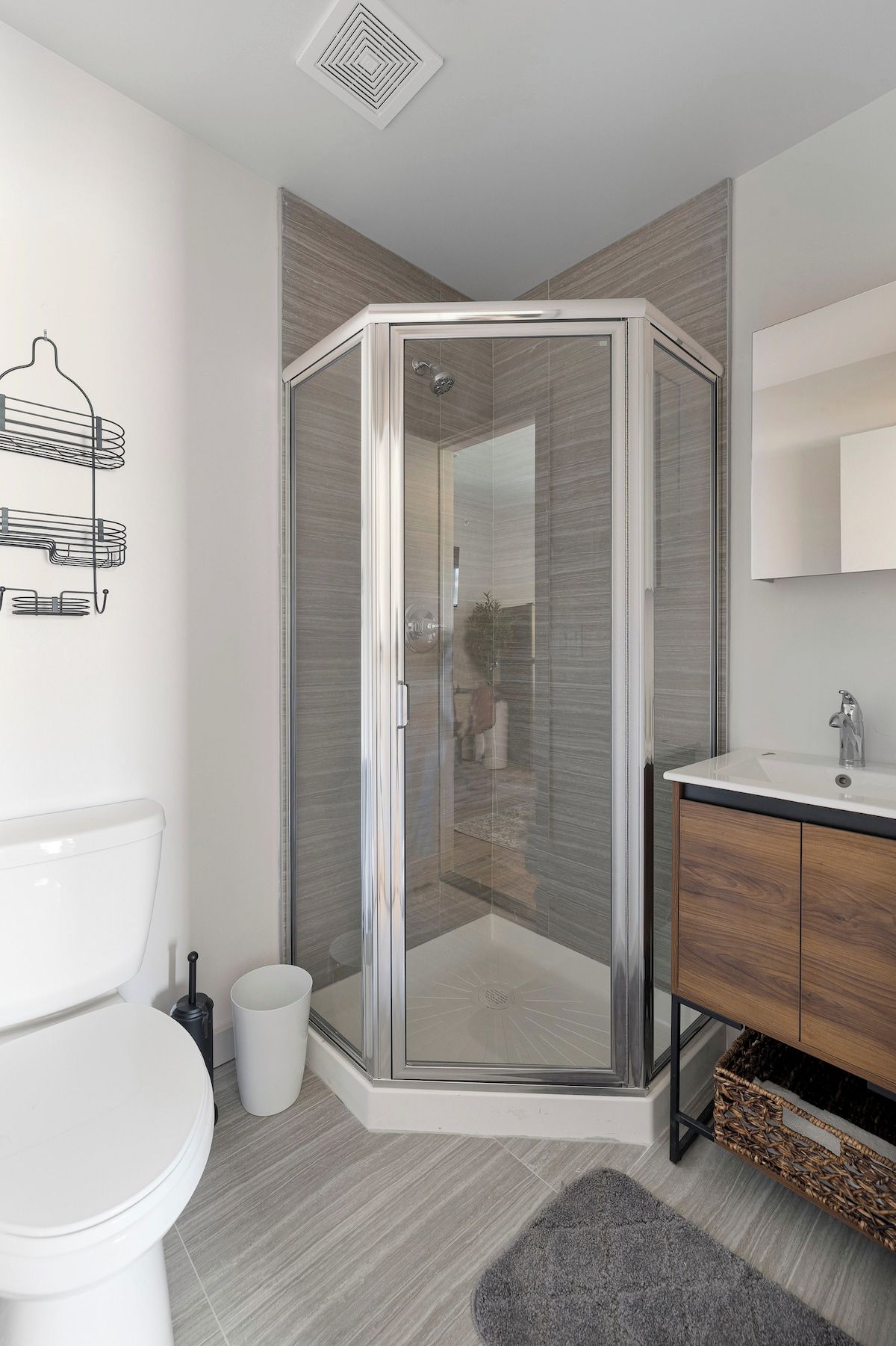 Une salle de bain moderne avec une douche à parois de verre, des toilettes, un lavabo avec un miroir et un porte-serviettes fixé au mur.