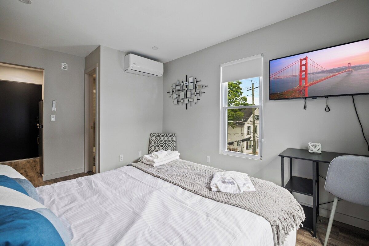 Een hotelkamer met een bed, een bureau, een stoel, een televisie en een raam met uitzicht op een brug.