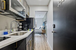 Cocina compacta con pileta, estufa y cafetera. Se ve una cama al fondo y una puerta con el número 304.