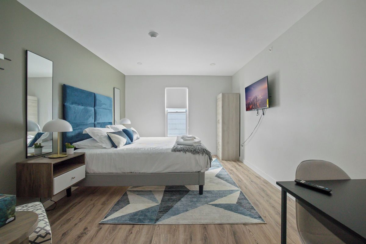 A modern bedroom with a bed, bedside table, lamp, and a TV on the wall.