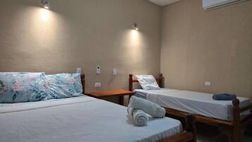A room with two single beds, each with a wooden frame and white bedding. There are wall-mounted lights above each bed, and an air conditioning unit on the wall.