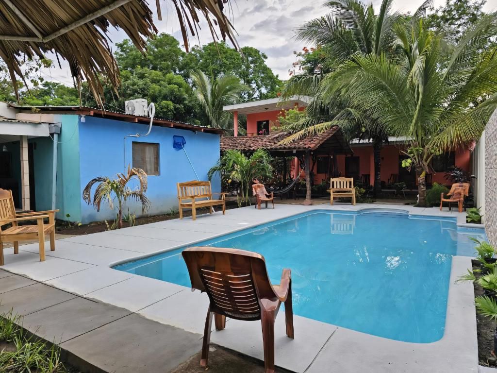 A swimming pool with chairs around it, a blue building, and palm trees.