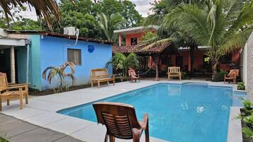 A swimming pool with chairs around it, a blue building, and palm trees.