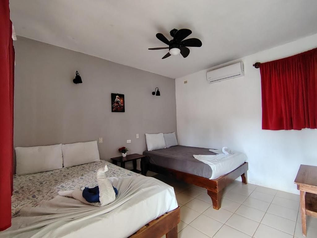 A bedroom with two beds, a ceiling fan, an air conditioning unit, and a red curtain.