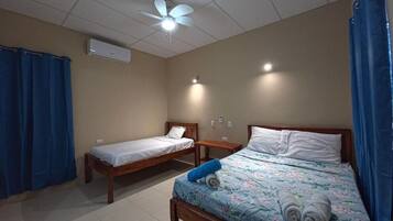 Una habitación con dos camas individuales, ventilador de techo, aire acondicionado y una pequeña mesa.