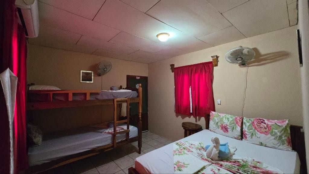 A dormitory room with bunk beds, a single bed, a fan, a clock, and a window with red curtains.