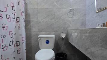 Un baño con inodoro, cortina de ducha, cubo de basura y espejo.