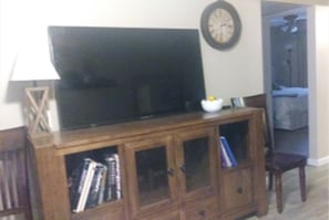 Un salon avec un téléviseur posé sur un meuble en bois, une horloge au mur et une porte donnant sur une autre pièce.