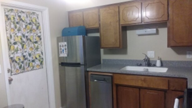 Una cocina con armarios de madera, un refrigerador de acero inoxidable, un lavavajillas y un lavaplatos.
