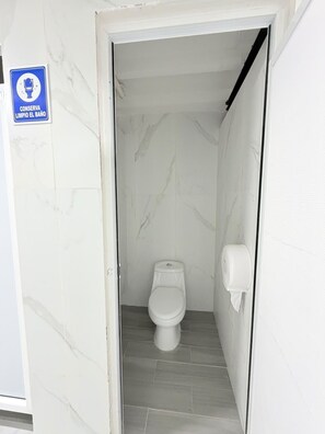 Un baño estrecho con un inodoro, un secador de manos y un letrero que indica mantener el baño limpio.