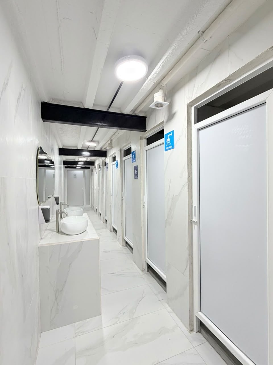 Un pasillo con varios baños, cada uno con una puerta blanca y un letrero azul que indica accesibilidad.