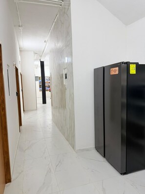 Un passadís amb terra de marbre, un refrigerador negre i una porta de fusta a l'esquerra.