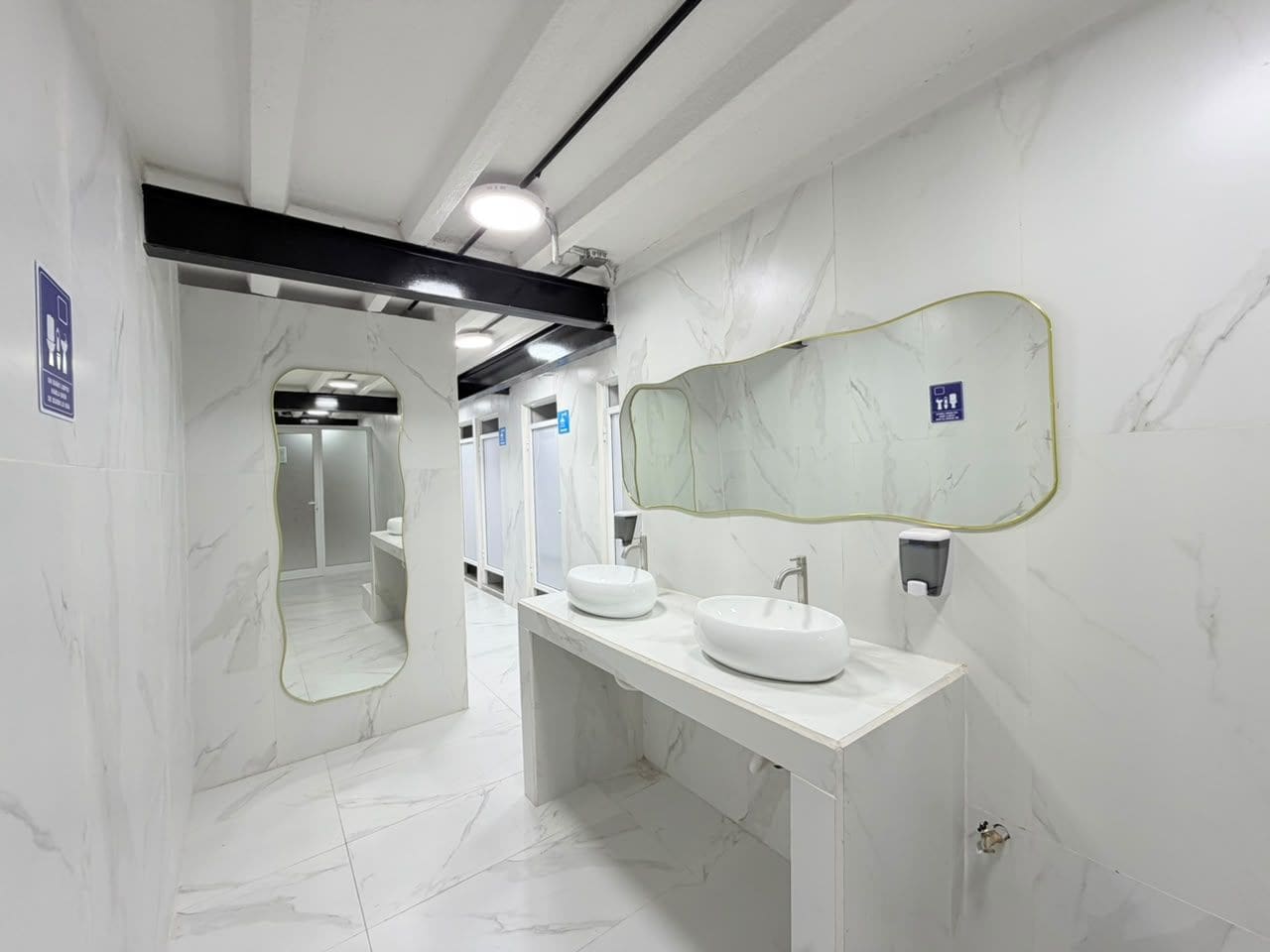 Un baño moderno con paredes de mármol, un espejo grande y dos lavamanos.