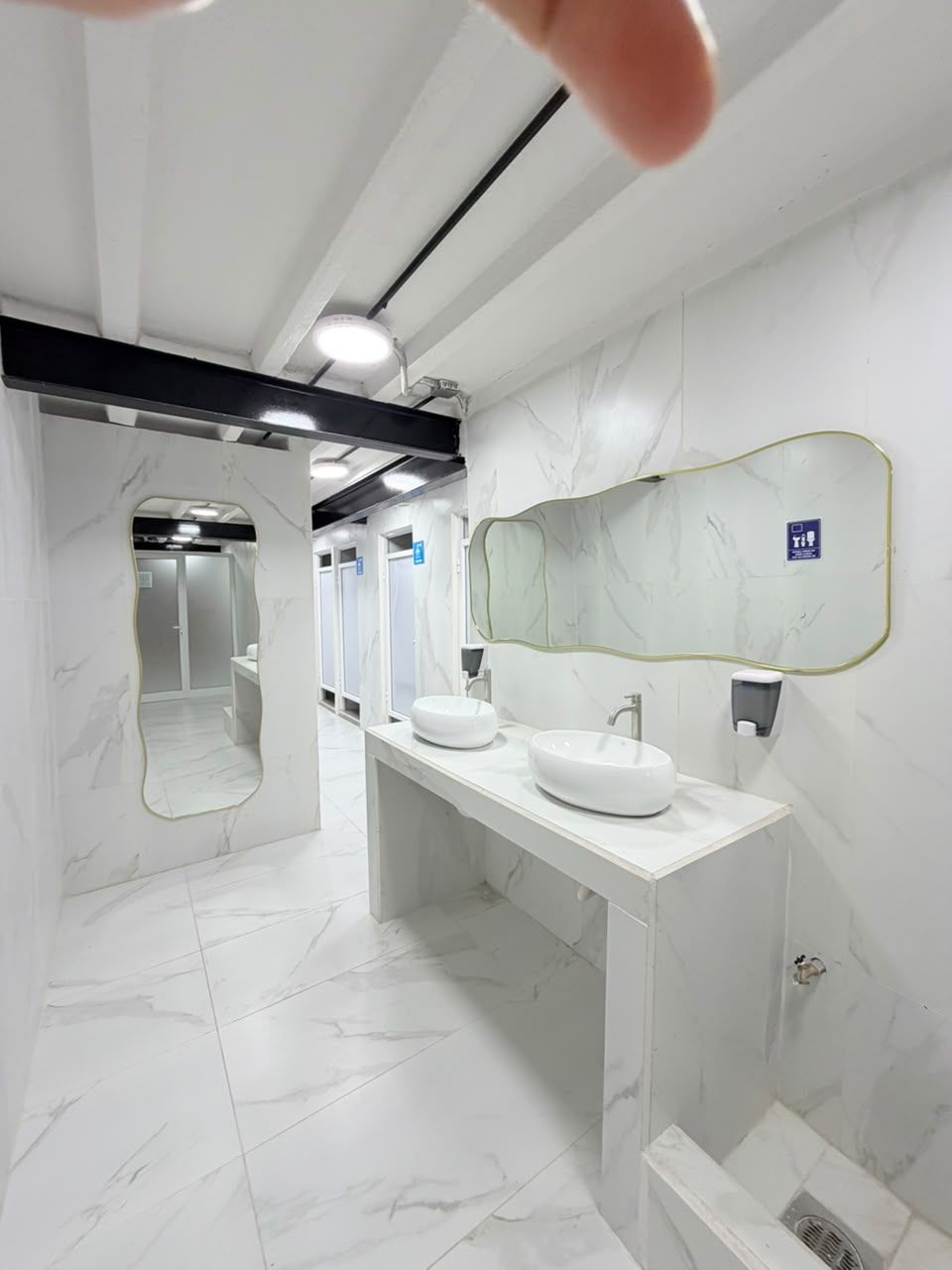 Un baño moderno con pisos de mármol, un espejo grande y dos lavamanos.