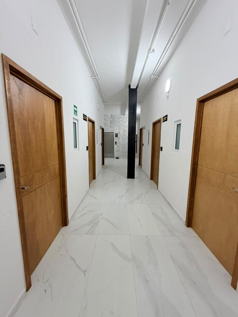 A hotel corridor with wooden doors, marble flooring, and a central elevator.