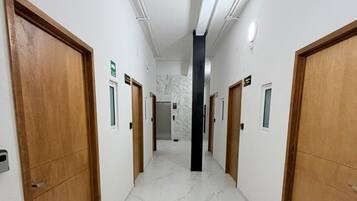 A hotel corridor with wooden doors, marble flooring, and a central elevator.