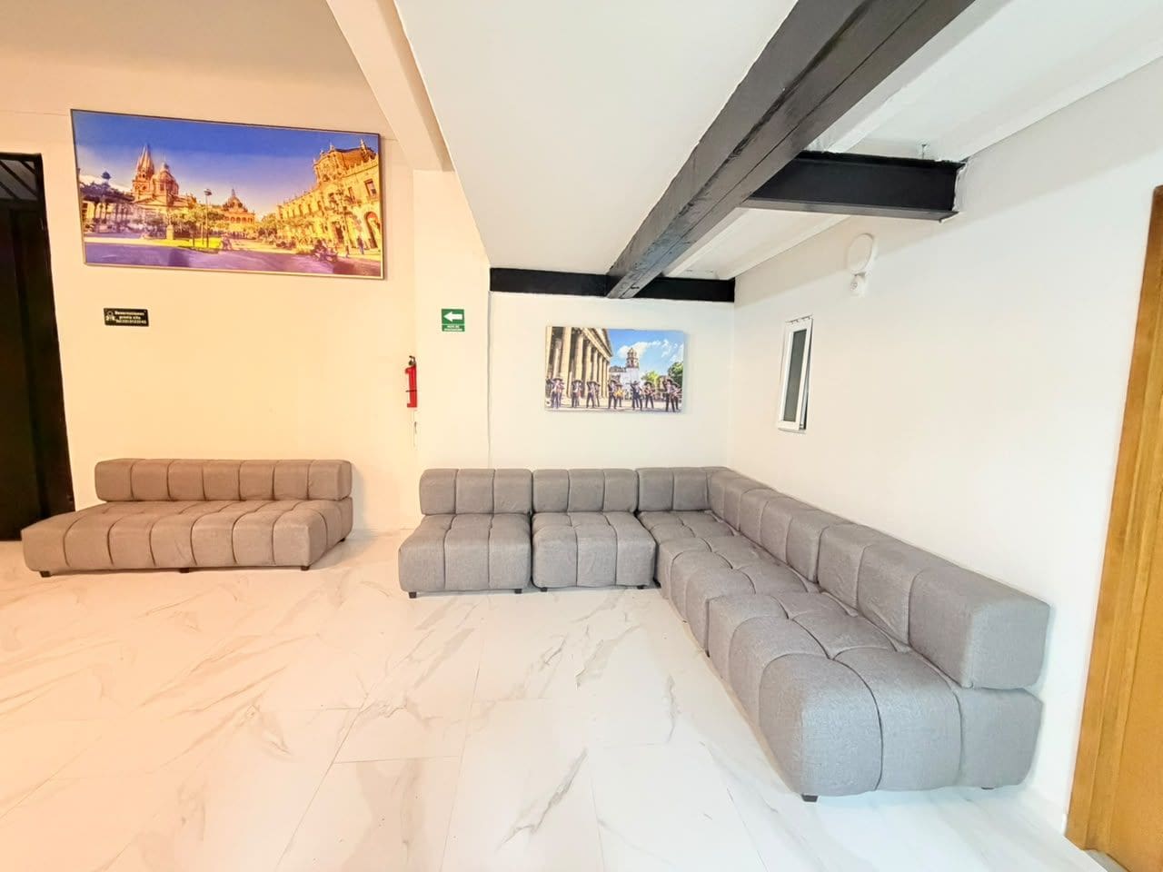 A modern living room with a sectional sofa, a flat-screen TV mounted on the wall, and a marble floor.