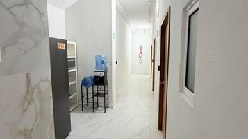 Un pasillo con paredes blancas y suelo de mármol, que conduce a una habitación con cama y ventana.