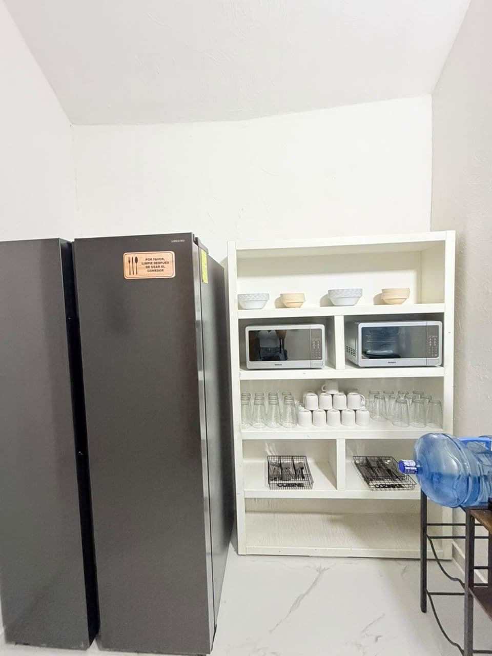 A kitchen with a black refrigerator, a microwave, and a white cabinet with shelves.