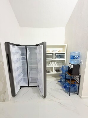 Una cocina con refrigerador, dispensador de agua y repisas con utensilios de cocina.