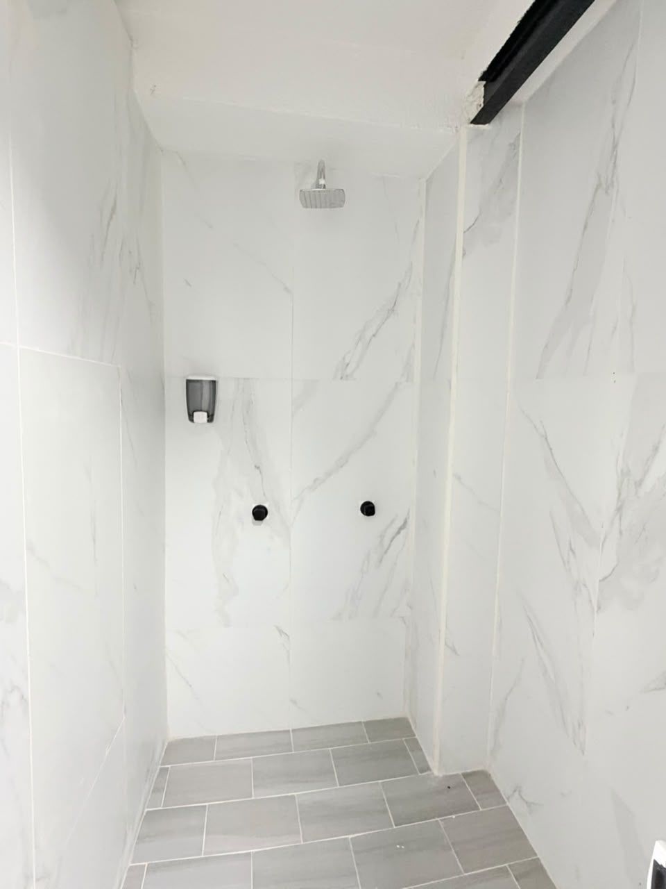 A small, enclosed shower area with white marble walls and grey tiles.
