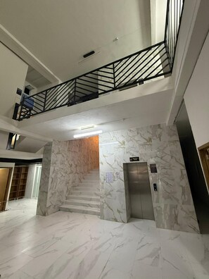 Un interior de diversos nivells amb paviment de marbre, una escala i un ascensor.