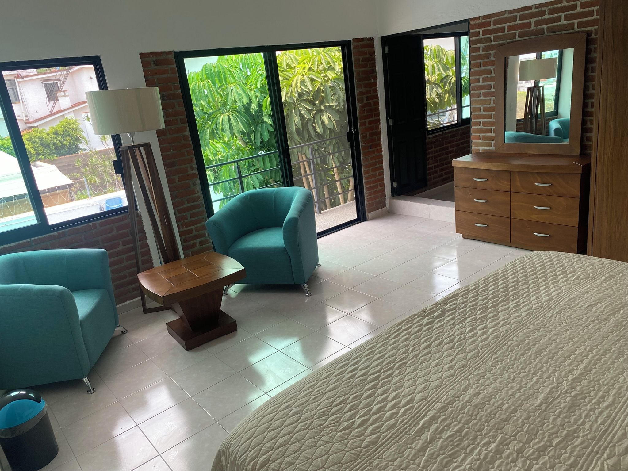A hotel room with a large bed, two armchairs, a small table, a dresser, and a mirror.