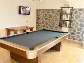 A pool table with a television mounted on the wall, a small wooden table, and a stone-patterned wall. - 5 bedrooms | Heated pool | Movie theater | Pool table - CASA ISELA (Cuernavaca)