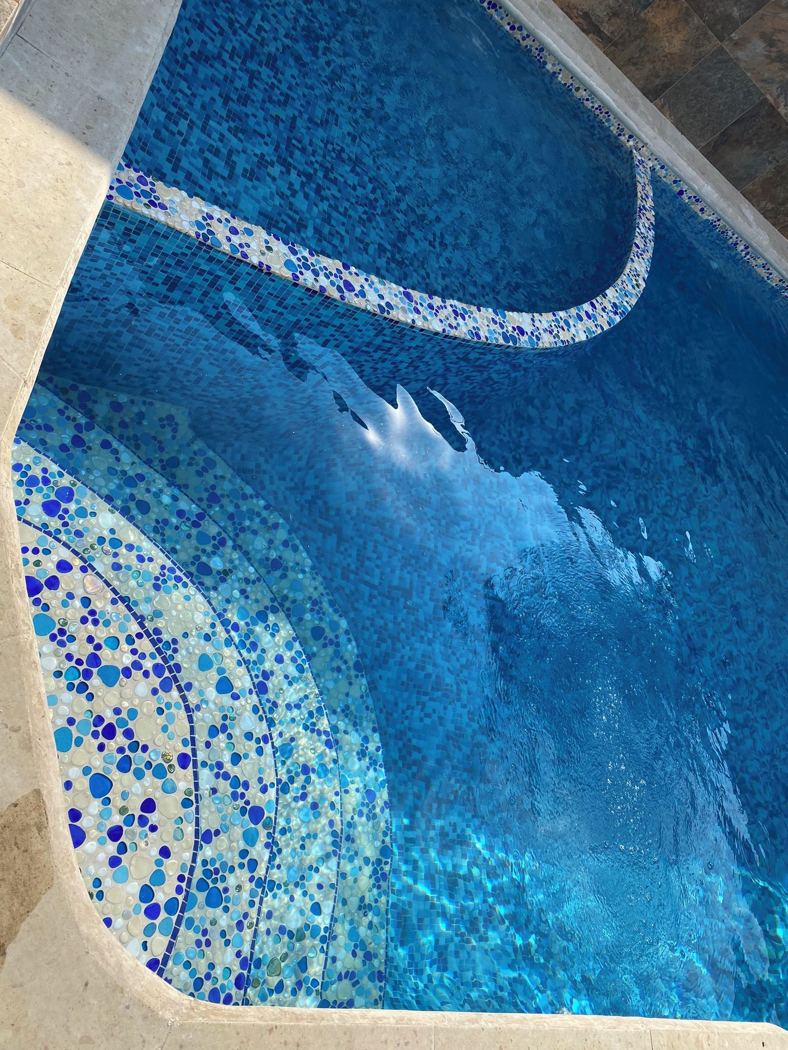 Una piscina con motivi a mosaico e bordo curvo.