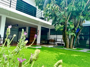 A modern building with a covered outdoor seating area, a well-maintained lawn, and a large tree. - 5 bedrooms | Heated pool | Movie theater | Pool table - CASA ISELA (Cuernavaca)