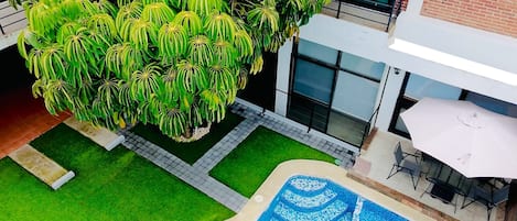 A rooftop garden with a swimming pool, a seating area, and a large tree.