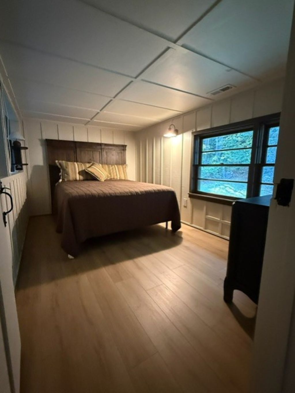 A bedroom with a bed, wooden flooring, a window with a view of trees, and a radiator on the wall.