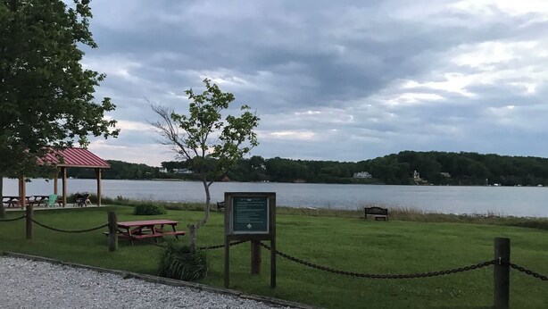 A lakeside park with picnic tables, a covered pavilion, and a signboard.