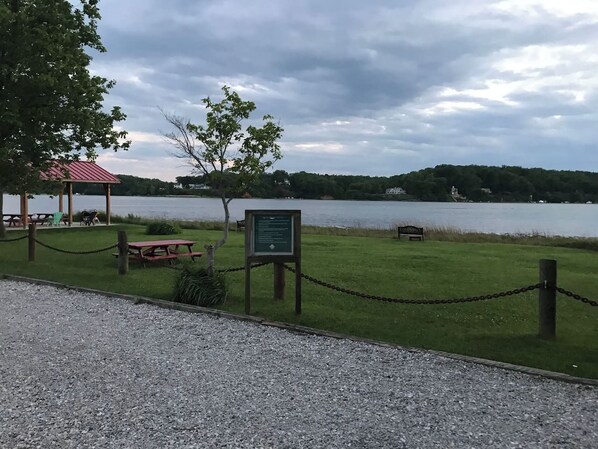 A lakeside park with picnic tables, a covered pavilion, and a signboard.