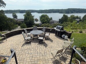 An outdoor patio with a round table and chairs, a grill, and a view of a lake.