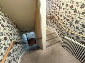 A carpeted staircase with a handrail, leading to a room with floral wallpaper.