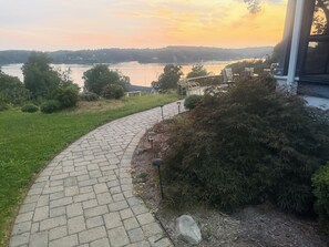 Un camí de maons corbat que condueix a una casa amb vista a un llac i a les colines llunyanes.