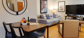 A living room with a sofa, a TV, a dining table with chairs, and a mirror on the wall. - Cozy 2BR on the Jackson Market Courtyard (Culver City)