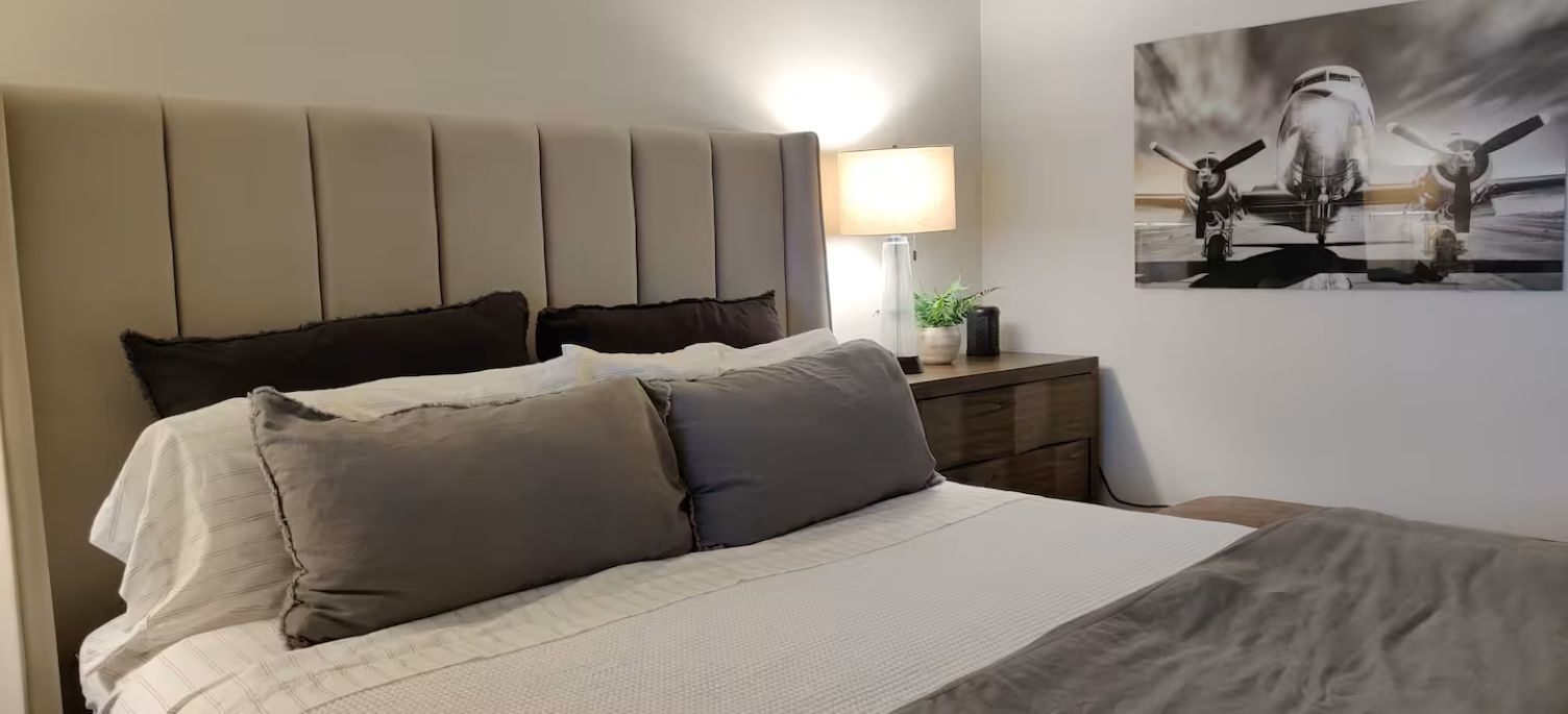 Uma cama com cabeceira, luminária de cabeceira e uma obra de arte na parede.