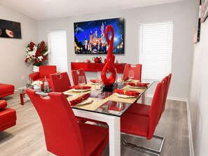 Un coin repas avec une table en verre, des chaises rouges et un tableau sur le thème d’un château accroché au mur.