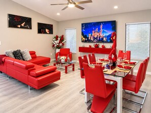 A modern living room with a red sofa, a glass coffee table, and a dining area with red chairs and a glass table. - Tremendous 4-bedroom house with AC in charming Kissimmee (Kissimmee)