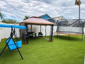 A backyard with artificial grass, a swing set, a covered seating area, and a trampoline. - Tremendous 4-bedroom house with AC in charming Kissimmee (Kissimmee)