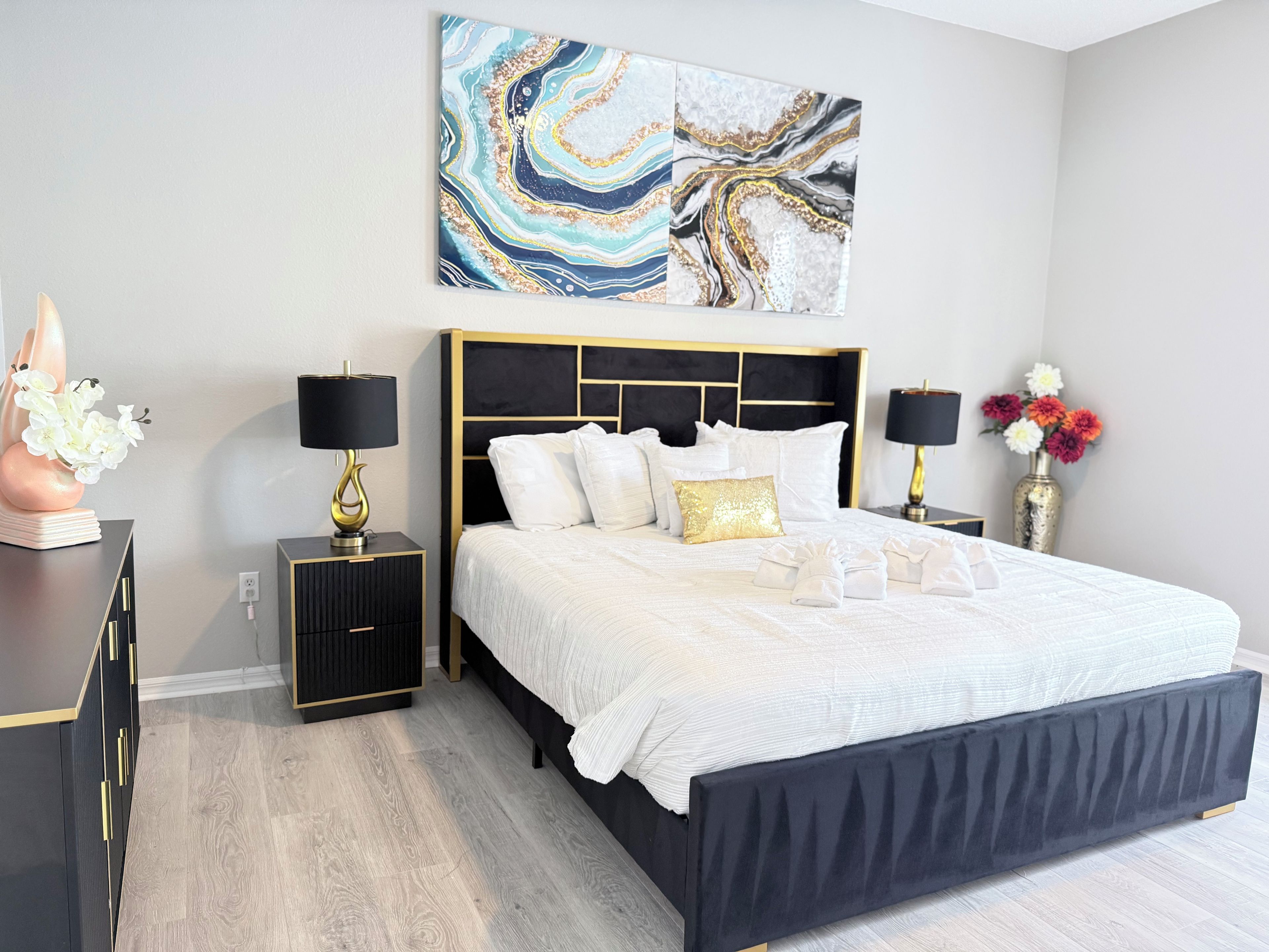 A modern bedroom with a large bed, two bedside tables, and a decorative wall piece.