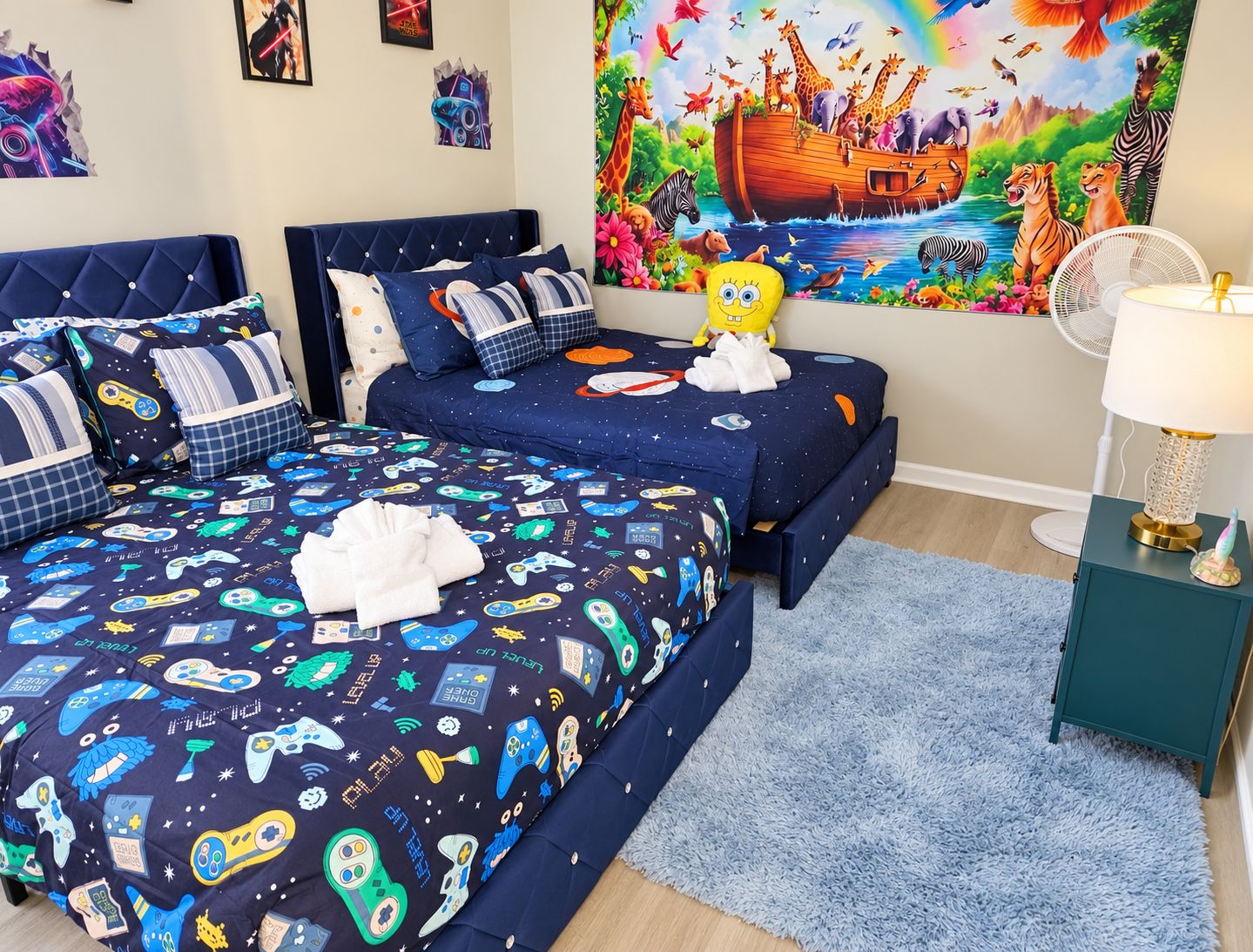 A bedroom with two beds, a colorful mural, a plush toy, and a bedside table with a lamp.