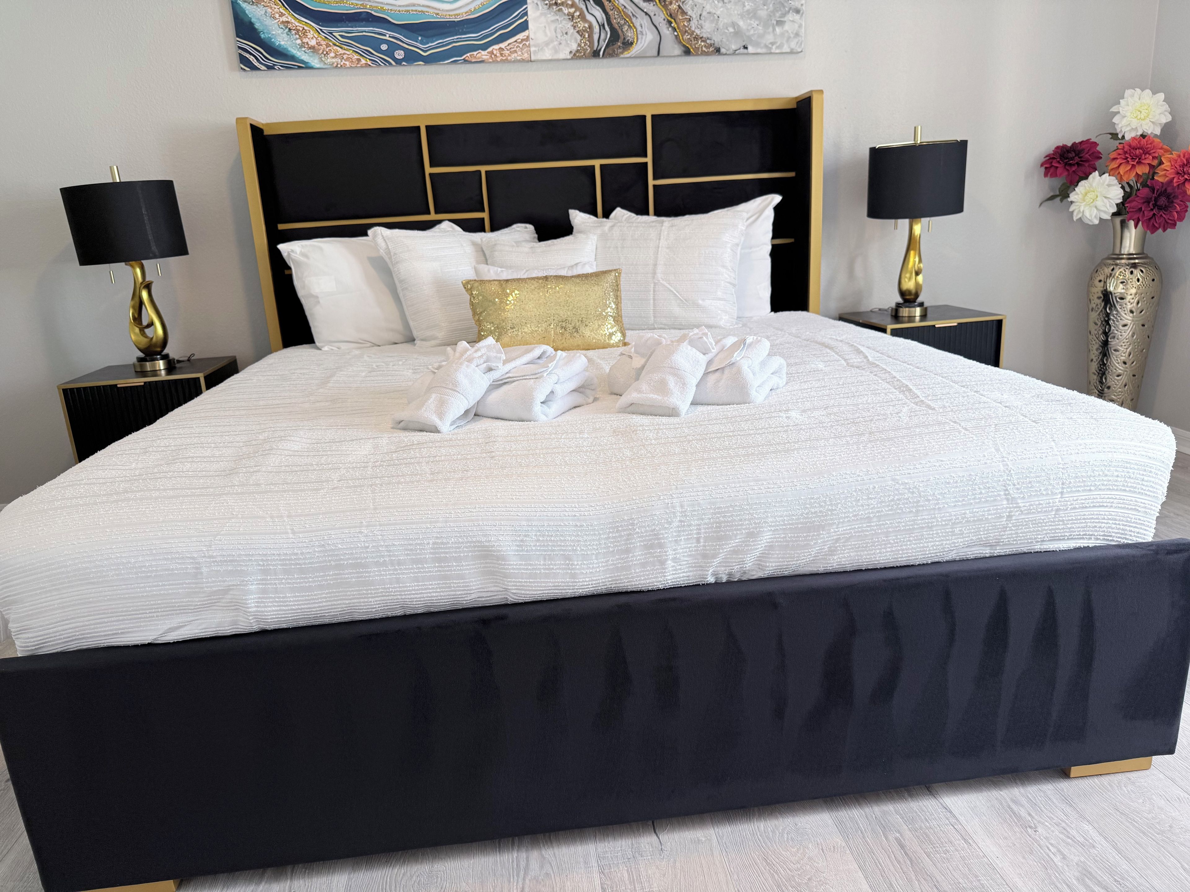 A hotel room with a large bed, two bedside tables, a headboard, and a wall-mounted artwork.