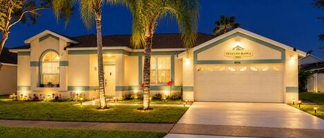 A two-story house with a garage, palm trees, and a well-lit front yard.