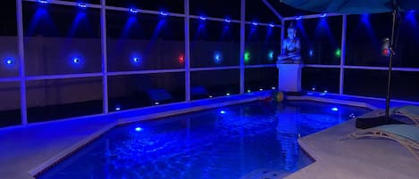An indoor swimming pool with a statue, surrounded by a covered area with blue lighting.