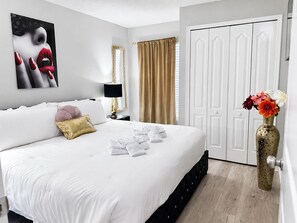 Une chambre d’hôtel avec un grand lit, une table de chevet avec une lampe, une armoire et un vase rempli de fleurs.